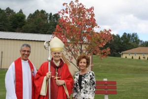 Fr. Michael Ferrick, Bishop Donald Trautman, and Sandy Florig pose in front of the newly planted tree at ECCHS.